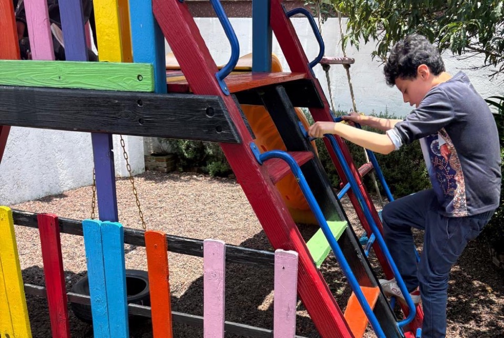 Alumno de primaria jugando en la estructura del patio escolar